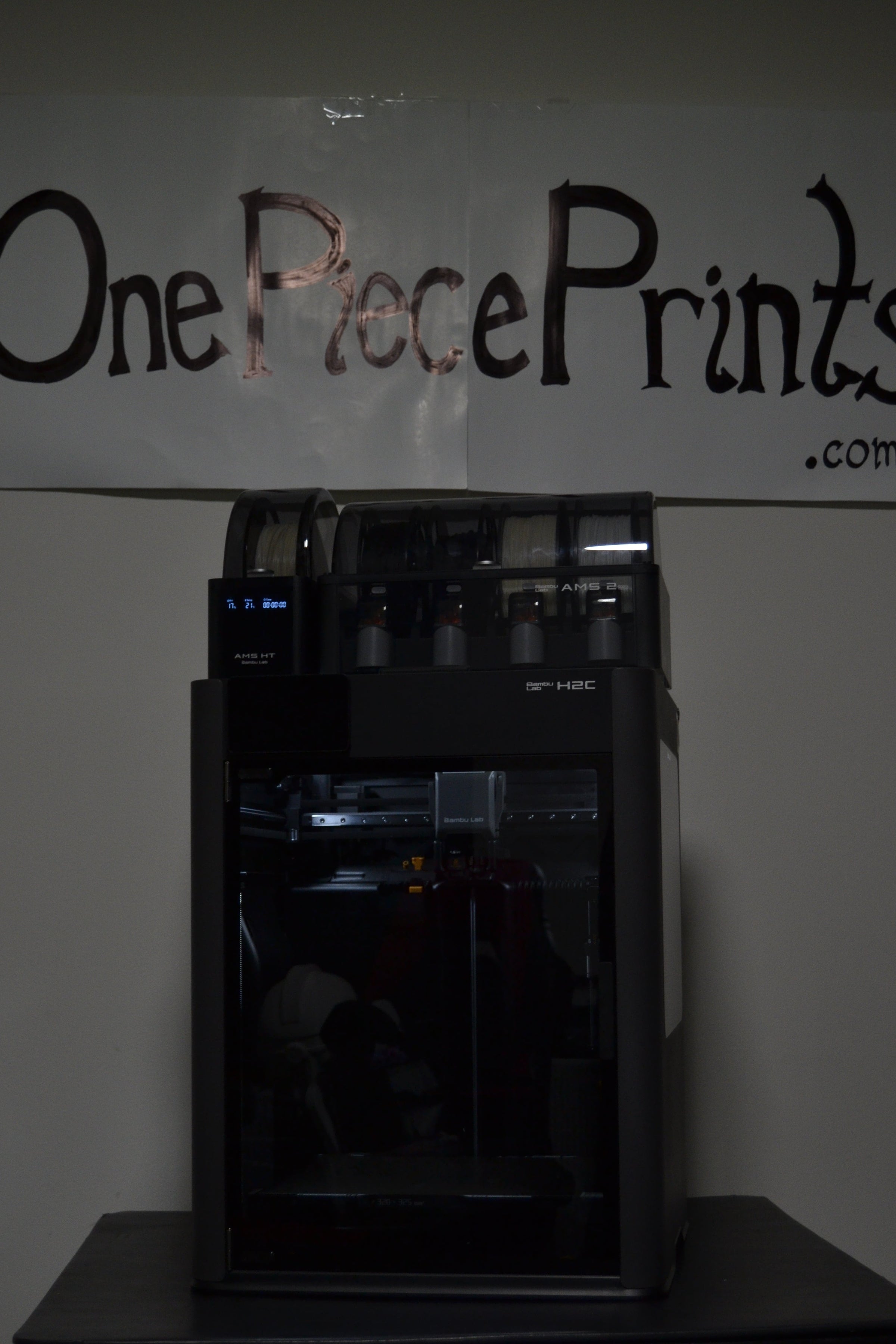 3D printer on a table with 'One Piece Prints' sign in the background